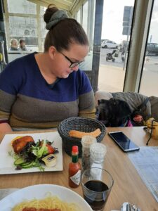 Lady with her dog at a table. Lady has a plate with salad before her
