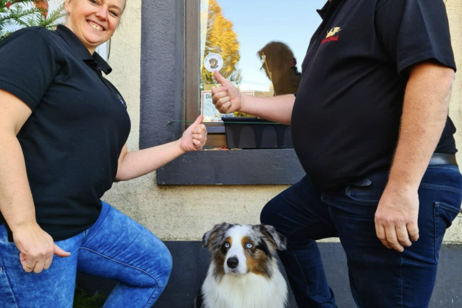 left: a woman pointing at the approved by jerom sticker. In the middle dog Zivko. At the right a man also pointing at the approved by jerom sticker
